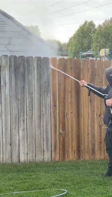 Pressure washing a grey cedar fence during a two-step restorative clean